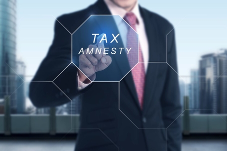 A businessman standing behind a screen that reads “tax amnesty” in reference to the tax amnesty period.
