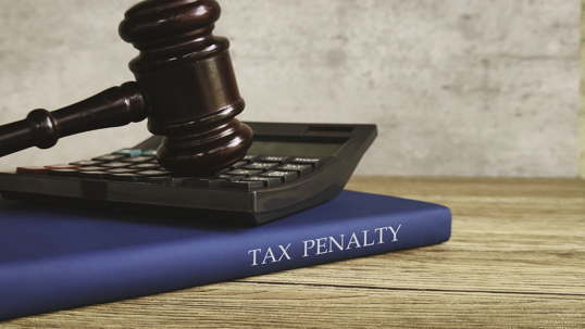 A gavel and calculator on a book titled TAX PENALTY representing financial and legal consequences.
